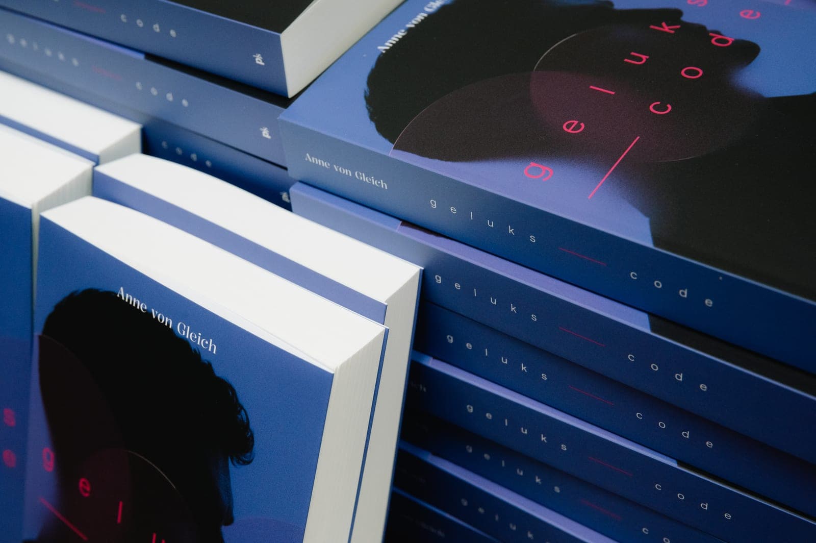 Stacks of copies of Gelukscode, with the silhouette and the title on the blue cover.