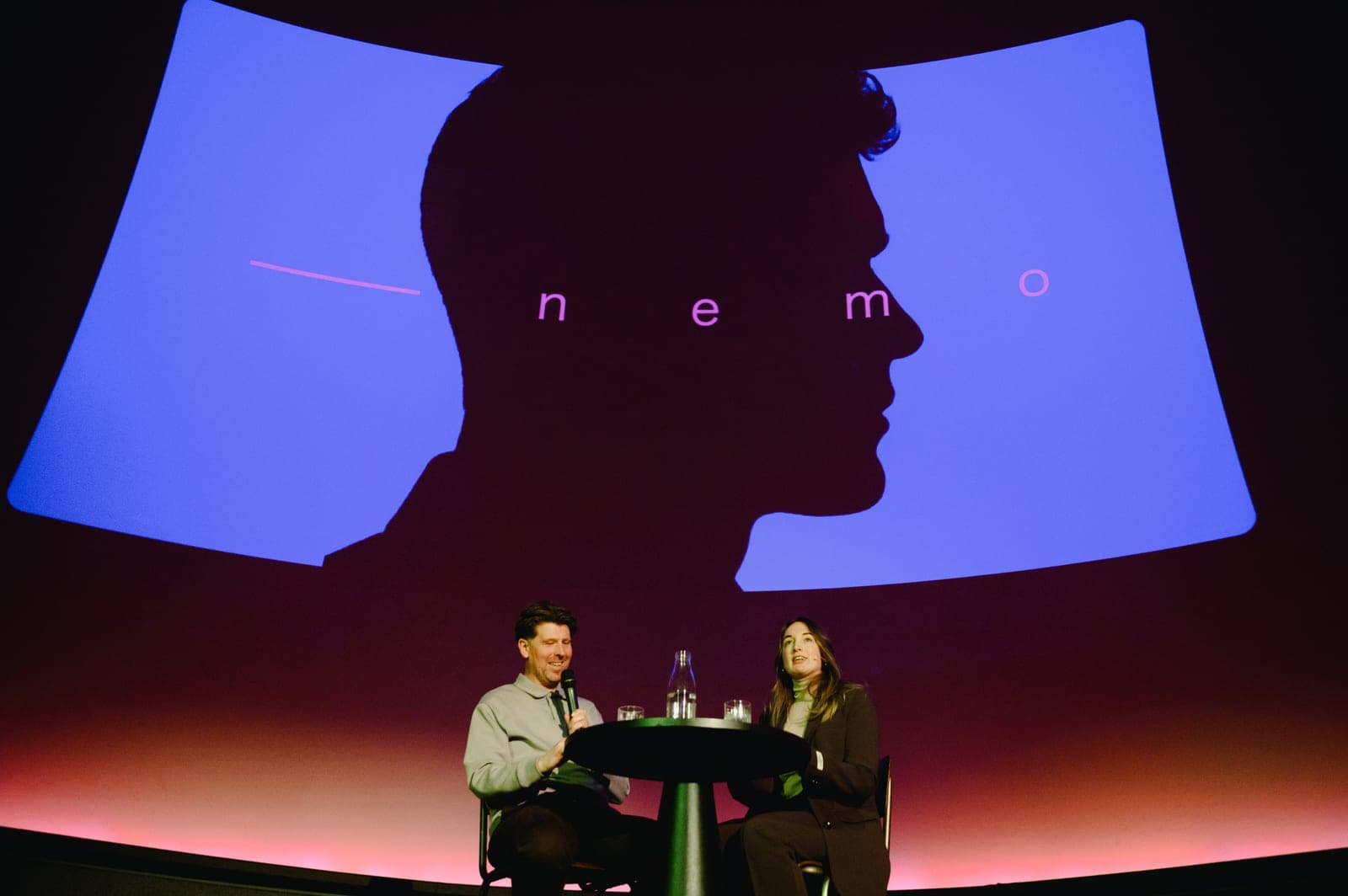 Two people in conversation at a table on the stage of DOT Groningen, under a projected silhouette from the book's design.